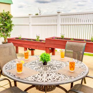 A charming patio setup with a decorative metal table, surrounded by chairs and adorned with glasses of iced tea, set against a backdrop of planter boxes and a white fence.