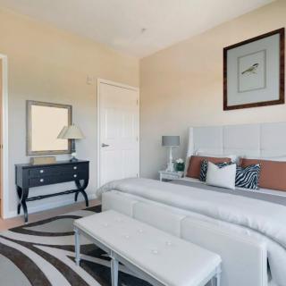 A modern bedroom with stylish decor, featuring a large bed, a dresser with a mirror, and elegant lighting.