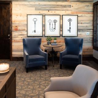 A cozy living room with two blue armchairs, a small round table, and key-themed artwork on a rustic wood-paneled wall.