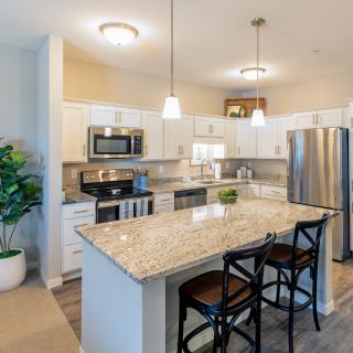 A modern kitchen featuring granite countertops, stainless steel appliances, and pendant lighting over an island with bar stools.