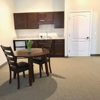 A minimalist dining area with a small table and chairs in front of a kitchenette.