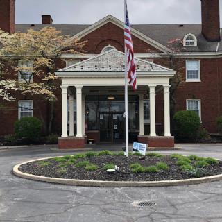 Front entrance of a brick building with columns and a flagpole.