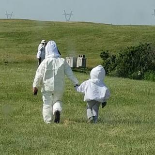 A parent and child walking hand-in-hand in protective beekeeping suits.