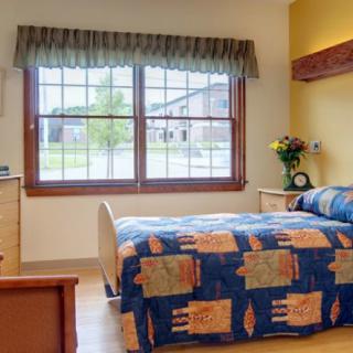 A cozy bedroom with a large window, featuring a bed and wooden furniture.