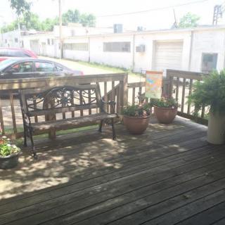 A sunny day on a wooden deck with a bench, potted plants, and a view of parked cars.