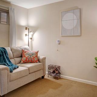 A cozy living room with a beige sofa, colorful cushions, a warm blanket, and decorative wall art.