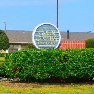 A sign reading 'Cedar Country' surrounded by greenery with a building in the background.