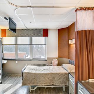 A modern hospital patient room featuring a bed, daylight from the window, and warm decor.