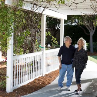A couple walks together outside under a gazebo in a garden.