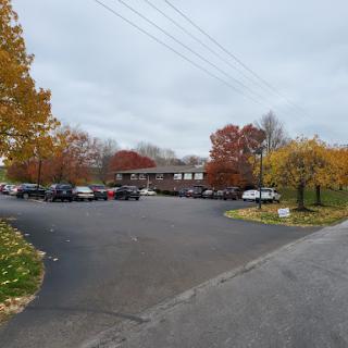 A view of a parking lot surrounded by autumn trees under an overcast sky.