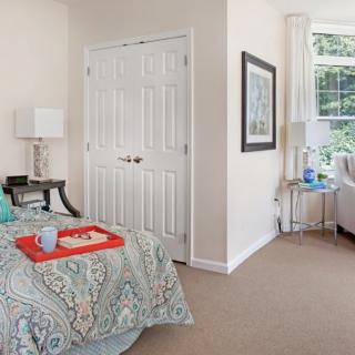 A cozy bedroom with a colorful bedspread, a tray on the bed, and a large window providing natural light.
