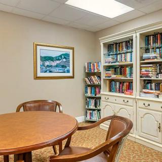 A cozy room with a circular wooden table and chairs, surrounded by bookshelves filled with various books.