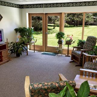 A cozy living room with rocking chairs, filled with natural light and indoor plants, overlooking a garden.