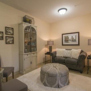 A cozy living room with vintage-style decor, featuring a sofa, cabinet, and an upholstered ottoman.