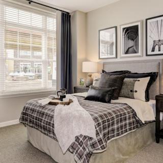 A cozy bedroom featuring stylish decor, complete with a comfy bed, decorative pillows, framed artwork, and a large window allowing natural light.
