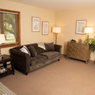 A cozy living room with a brown sofa, two floor lamps, and framed artwork on the walls.