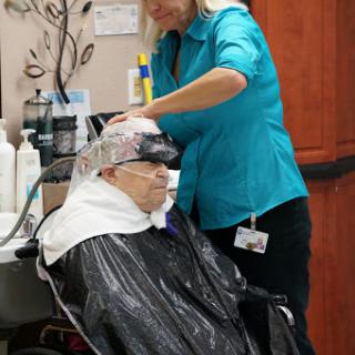 A stylist provides a hair treatment to a senior citizen in a salon setting.