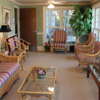 A cozy living room featuring rattan furniture, a glass coffee table, and large windows.