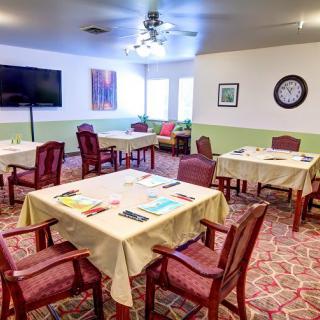 A well-organized dining room with multiple tables and chairs, featuring a television, artwork, and a wall clock.