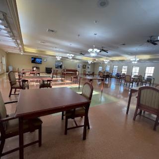 A spacious and well-lit dining area designed for community gatherings, featuring wooden tables and chairs.