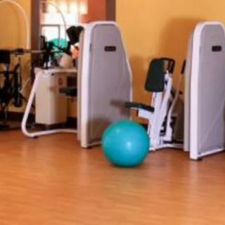 A gym with various exercise equipment and an exercise ball on the wooden floor.