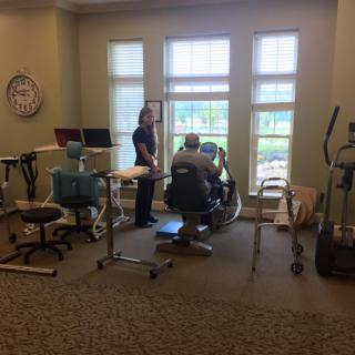 A physical therapy session in progress with a therapist assisting a patient by the window.