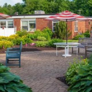 A peaceful garden patio with outdoor seating, a striped umbrella, and lush greenery.