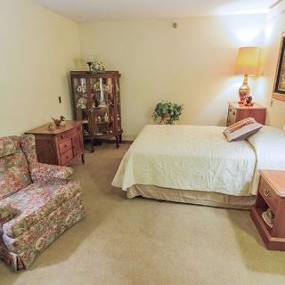 A cozy bedroom featuring vintage decor with a bed, armchair, and cabinet.