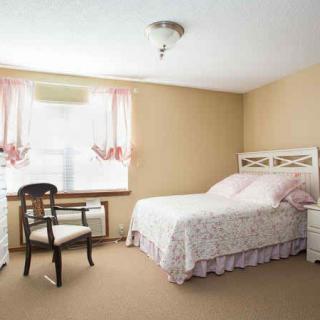 A cozy bedroom with a bed, chair, and window adorned with pink curtains.