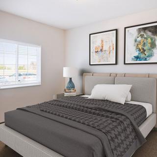 A modern bedroom with a neatly made bed, artwork on the wall, and a bedside lamp.
