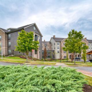 A modern apartment complex surrounded by well-maintained landscaping and greenery under a cloudy sky.