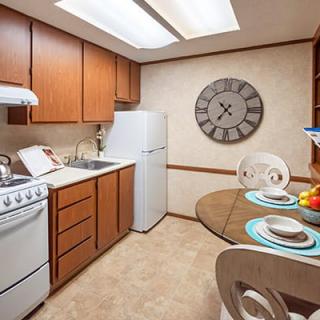 A cozy apartment kitchen with wooden cabinets, a dining table set, and a large wall clock.