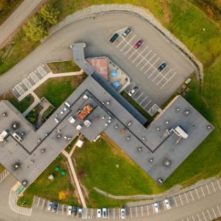 Aerial view of a modern building with a spacious parking lot surrounded by green areas.