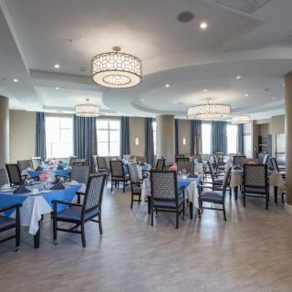 An elegant dining room with well-arranged tables and chairs, adorned with chandeliers and large windows.