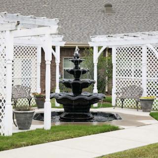 A serene garden scene featuring a black fountain surrounded by white trellises and seating areas.