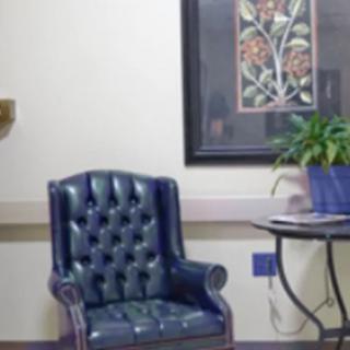 A cozy waiting area with a blue upholstered chair, a table with a plant, and framed artwork on the wall.