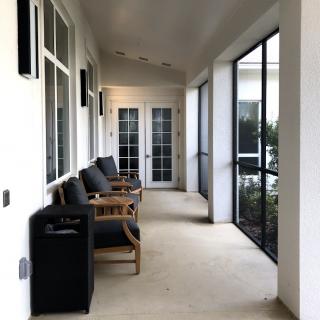 A covered porch with chairs and large windows, leading to double doors.