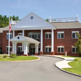 A brick building with a columned entrance and an American flag by the driveway.