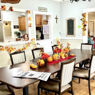 A cozy dining room decorated with fall-themed decor, featuring a table adorned with pumpkins and autumn leaves.