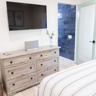 A contemporary bedroom featuring a flat-screen TV mounted on the wall, a stylish dresser, and access to a bathroom.