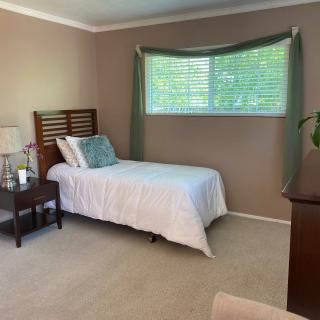 A simple bedroom with a single bed, nightstand, and window with green curtains.