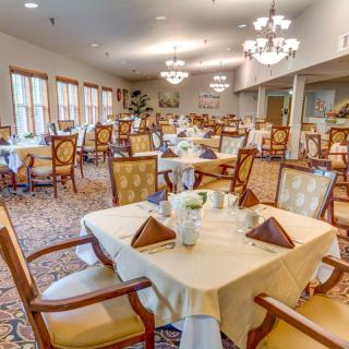 An elegant dining room with neatly arranged tables and chairs, illuminated by chandeliers.