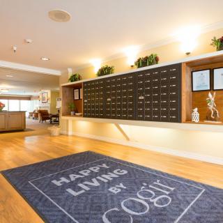 A welcoming lobby area featuring mailboxes and a 'Happy Living by Cogir' welcome mat.