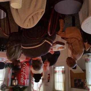 A group of people engaged in conversation inside a cozy cafe with a Coca-Cola sign on the wall.