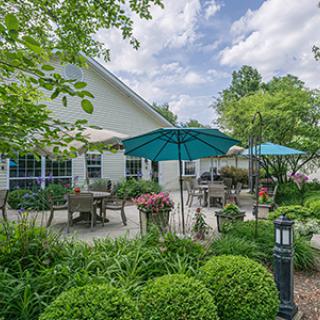 A beautiful outdoor patio area with tables, chairs, and umbrellas surrounded by lush greenery.