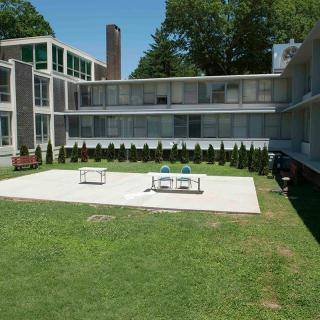 A modern residential building with a central courtyard featuring outdoor seating and surrounded by a green lawn.