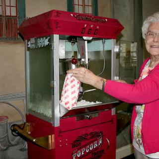 An elderly woman serves popcorn from a vintage popcorn machine.