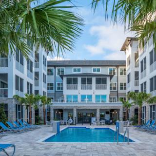 A serene view of a modern apartment complex featuring a swimming pool surrounded by palm trees.