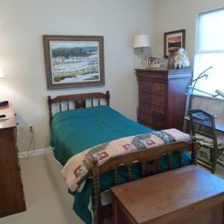 A cozy bedroom with a single bed, dresser, and artwork on the wall.