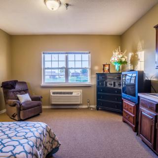 A cozy bedroom with an armchair, dresser, and television next to a window.